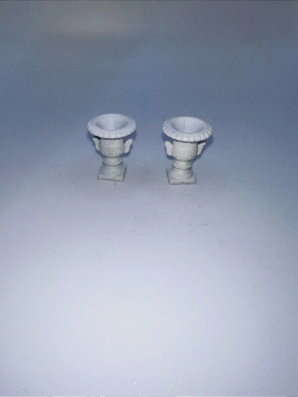Miniature Medici-style vases feature a classic white finish and ornate pedestal